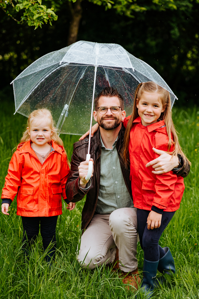Vater sitzt lächelnd mit Töchtern unterm Regenschirm
